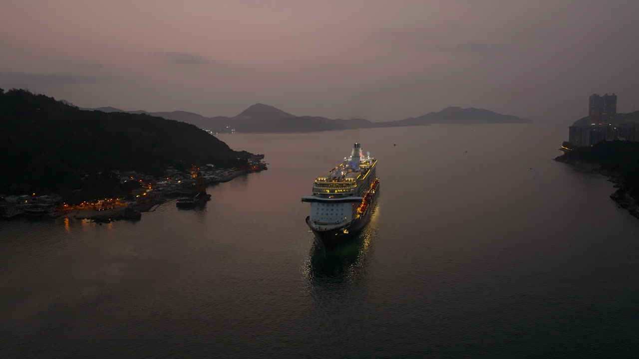 un crucero iluminado por las luces mientras se acerca a hong kong al amanecer.