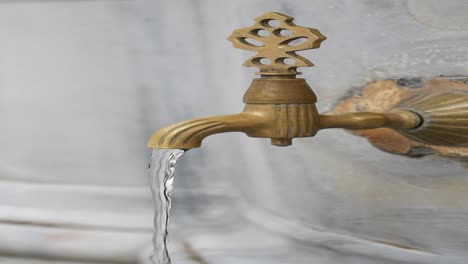 close-up of a brass faucet with ornate handle, water flowing