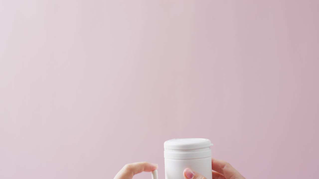 video de manos sosteniendo una caja de pastillas blancas y una pastilla blanca sobre un fondo rosa con espacio para copiar.