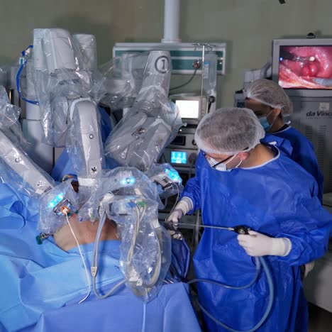 surgeon specialist carries out surgery with the help of robotic arm. female assistant helping the surgeon. screen showing the place of surgery at the backdrop