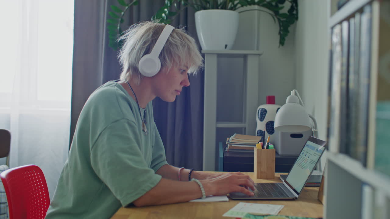 Focused Girl in Headphones Typing on Laptop at Desk in Home Office