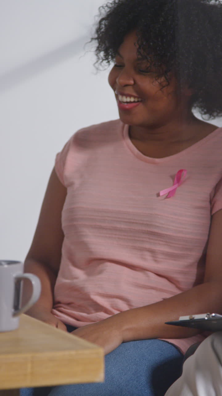 Vertical Video Of Smiling Mid Adult Woman Wearing Pink Breast Cancer Awareness Ribbon Meeting And Talking At Therapy Support Group For Cancer Treatment Patients With Counsellor