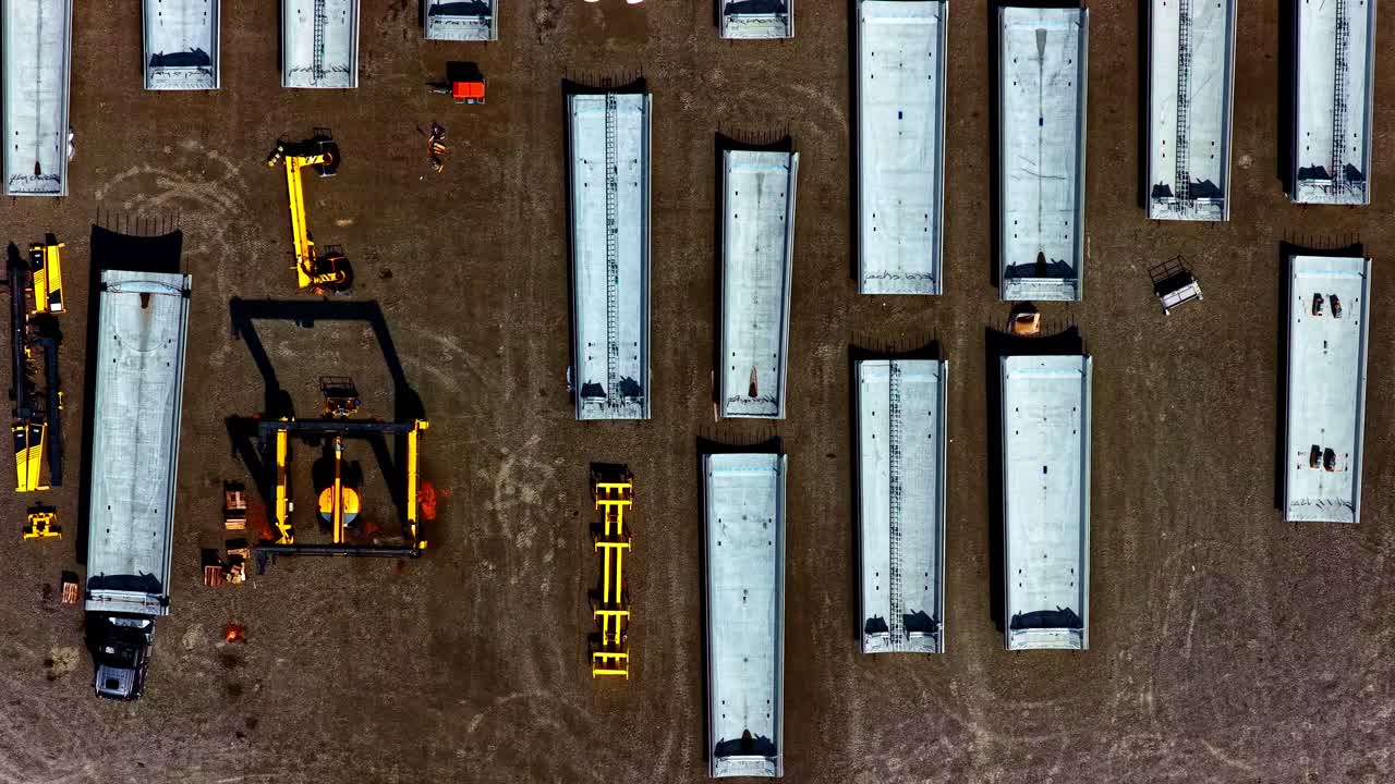 Bird's eye view of concrete sections of a wind turbine tower and a gantry crane, showing the logistics of a wind farm project. Aerial top-down forward