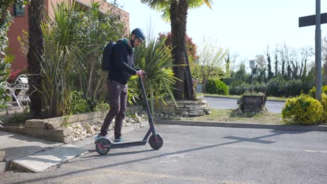 hombre europeo con casco y mochila viaja en un scooter eléctrico en un día soleado