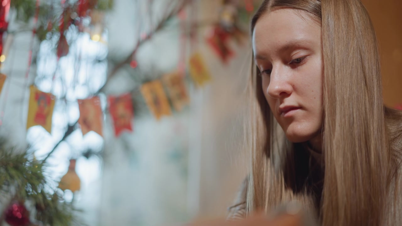 Teen girl arranging advent calendar by window, warm bokeh lights, pine branches, sweater, focused expression, closeup angles showing hands and handmade paper flags, cozy indoor holiday atmosphere