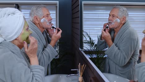 Old-senior-couple-man-and-woman-doing-morning-hygiene-procedures-and-looking-into-a-mirror