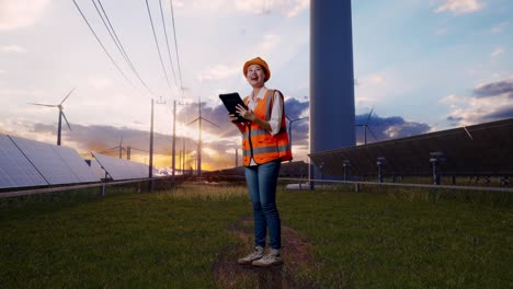 full body side view of asian female engineer with safety helmet looking at the tablet in her hand and looking around with solar panel and wind turbines
