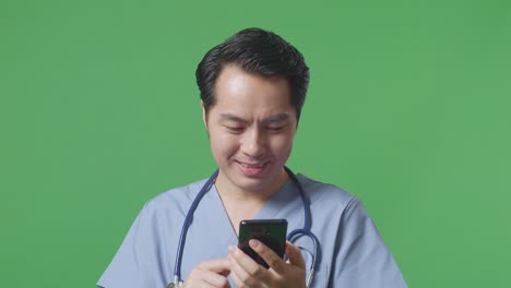병원에서 녹색 화면 배경에 서 있는 스마트폰을 사용하여 스테토스코프를 가진 아시아 남성 의사의 클로즈업