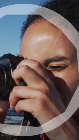 Animación-De-Círculos-Sobre-Una-Mujer-Birracial-Tomando-Fotos-Con-Cámara-Junto-Al-Mar