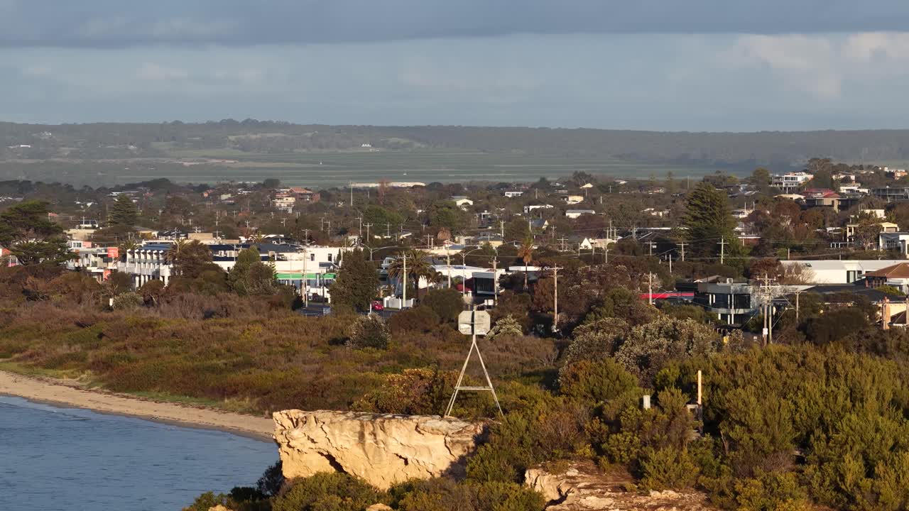 Drone pans from rocky clifftop to coastal town, golden hour lighting, wide landscape perspective