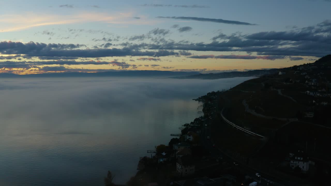 sobrevolando la orilla del lago léman con el tren suizo pasando y desapareciendo en la niebla al atardecer