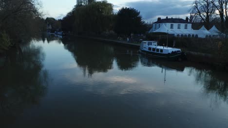 aerial proximity flight over the isis river in oxford, overlooking a white house, people with kids walking, a park and boats on the shoreline. dolly in