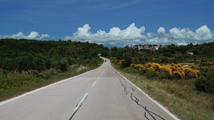 Vista in avanti guidando su una strada di campagna circondata da vegetazione verde verso la lontana isola di Pag, Croazia