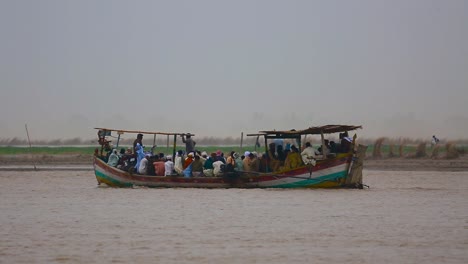 riesige gruppe asiatischer pakistaner mit damen und motorrädern, die mit einem boot über einen fluss fahren, menschen im schutz des bootes