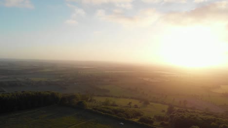 aerial cinematic shot of english country road in green countryside during sunset with bright orange glow-1