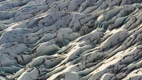 zoomed lifting shot of wavy ice on a frozen glacier illuminated by sunlight