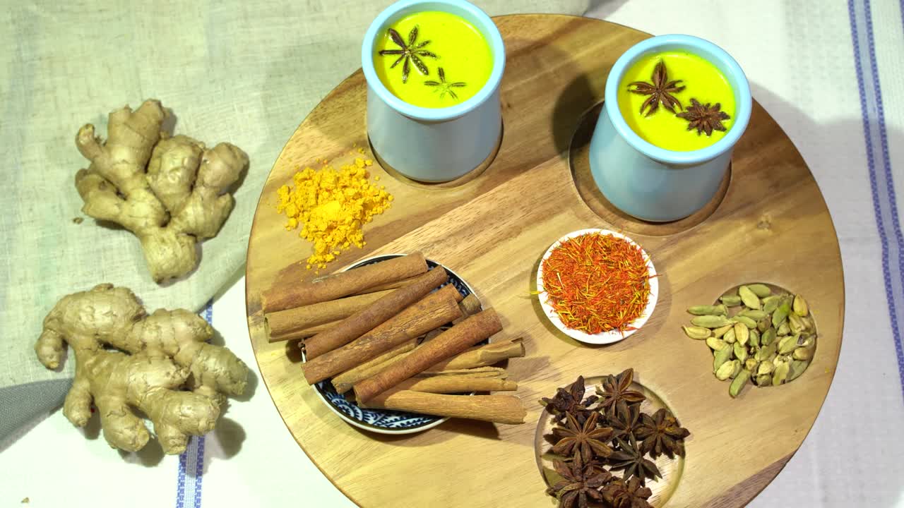 황금 우유를 만드는 재료: 커머릭, 카네몬, 애니즈, 스타 애니즈, 진저, 골든 우유를 나무 테이블 위에 세라 컵에 넣고 360도 원형으로 움직입니다.