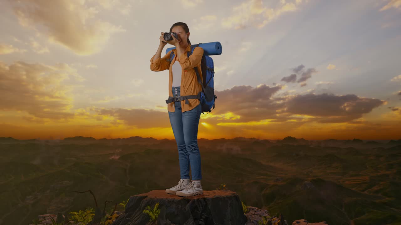 vista lateral completa del cuerpo de una excursionista asiática con mochila de montañismo usando una cámara tomando una foto mientras está de pie en la cima de la montaña durante la hora del atardecer