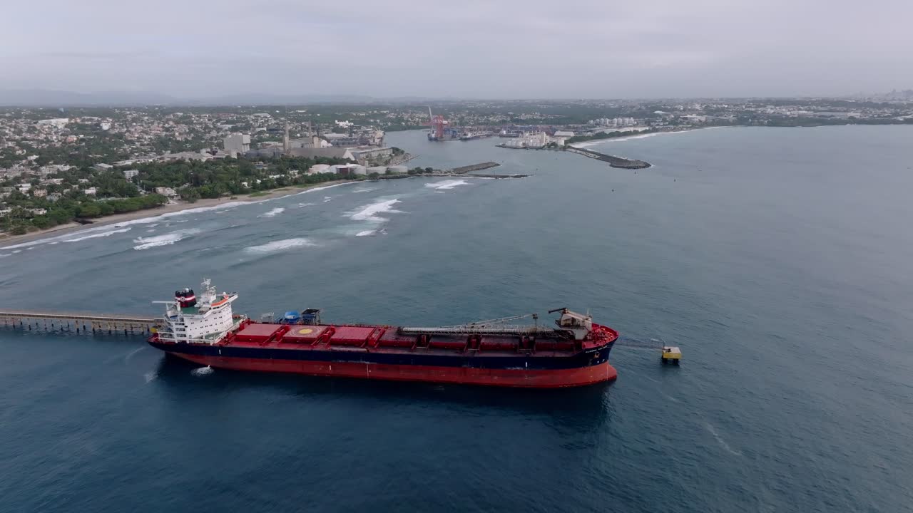Aerial approaching shot of docked oil tanker at port of Haina. Coastline of city in Dominican Republic. Supply Island with oil. Wide shot.