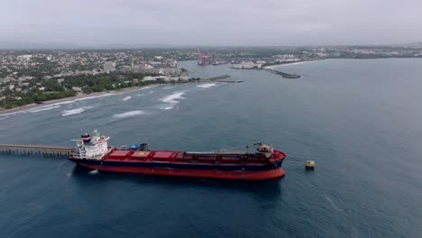 aerial approaching shot of docked oil tanker at port of haina. coastline of city in dominican republic. supply island with oil. wide shot.
