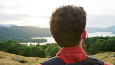 A-young-adult-Caucasian-man-standing-at-the-summit-admiring-the-view-during-a-mountain-hike,-close-up,-back-view