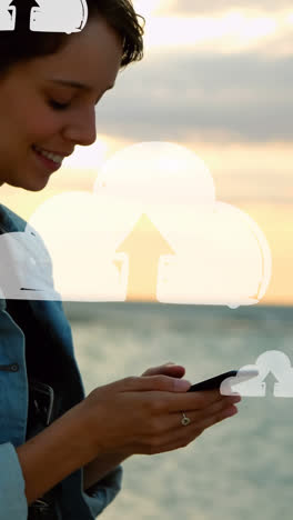 animación de nubes sobre la sección media de una mujer biracial usando un teléfono inteligente en la playa