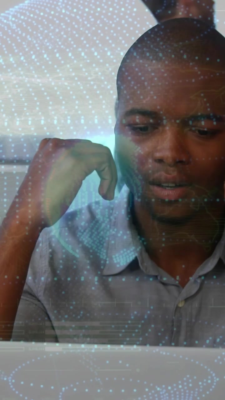 Glancing down, typing man wearing gray shirt at office, analyzing laptop data with digital globe