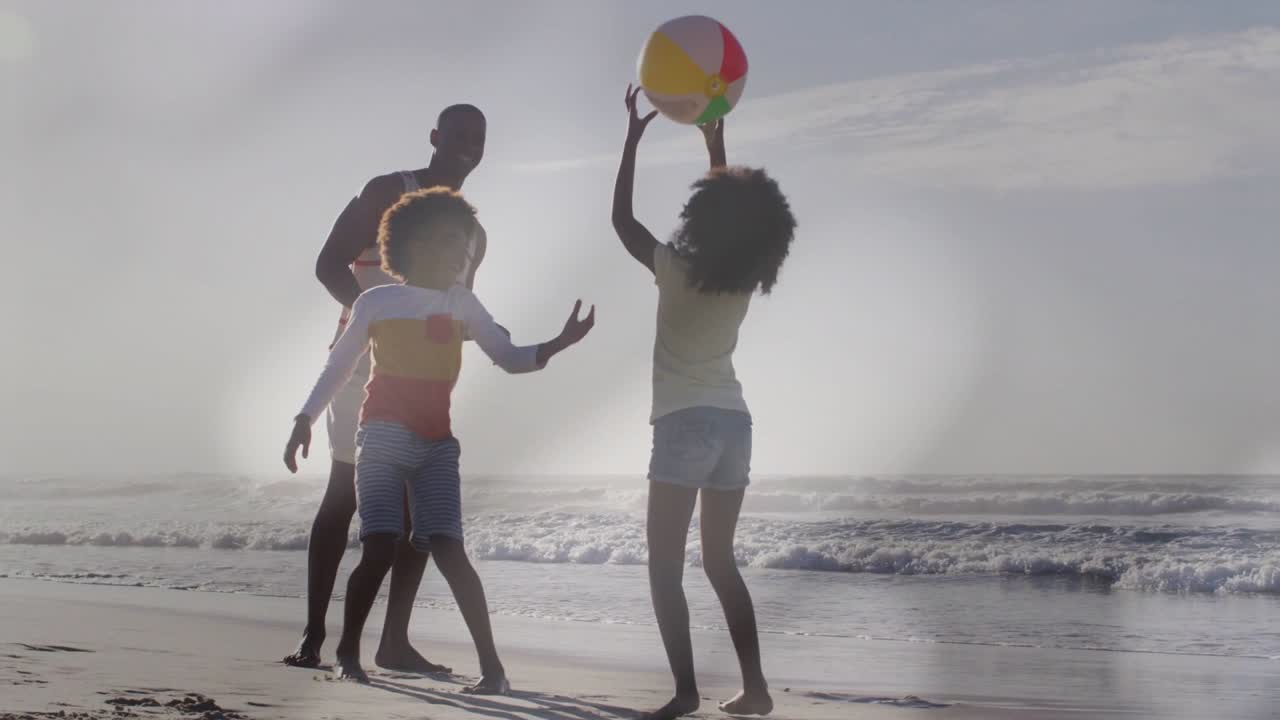 Father watching as children catching and passing beach ball being tossed, backlit bonding marketing