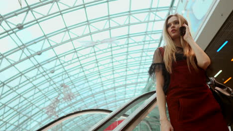 a beautiful girl descends the escalator and talks on the phone in the mall.