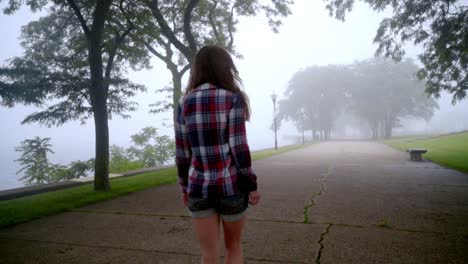 mujer joven caminando en la niebla del parque. niña caminando en los árboles de niebla