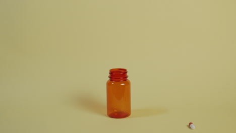 slow motion wide shot of a pill as it falls vertically towards an open pill bottle and bounces off the rim