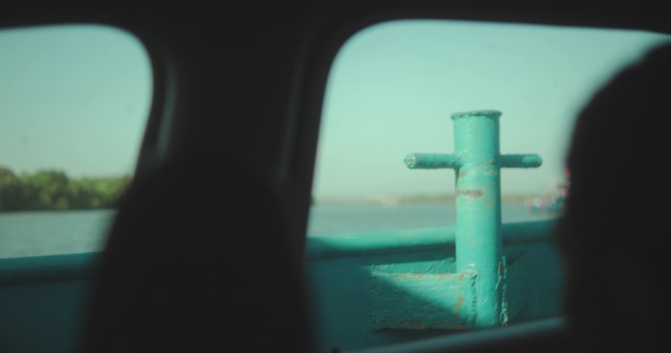 Vista cinematografica dall'interno di un traghetto in movimento o di una chiatta fluviale, che cattura l'atmosfera di viaggio lento, il trasporto e il sereno paesaggio lungo l'acqua.