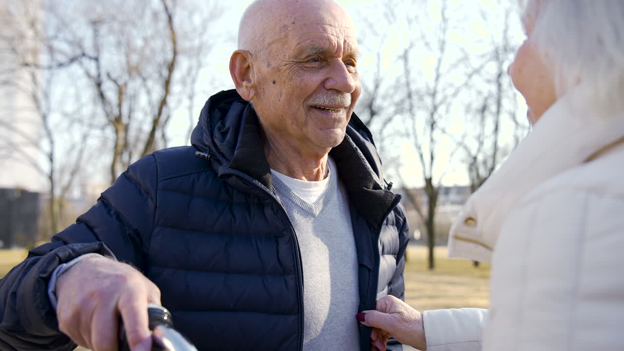 Close-up view of a senior man holding a bike, laughing and talking with her wife in the park on a winter day