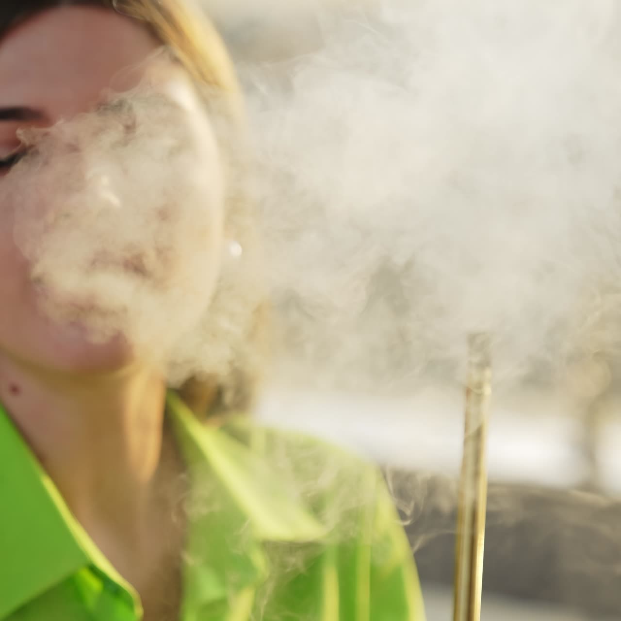 Young beautiful female producing thick white smoke from smoking nargileh. Brunette looking into camera while smoking. Close up