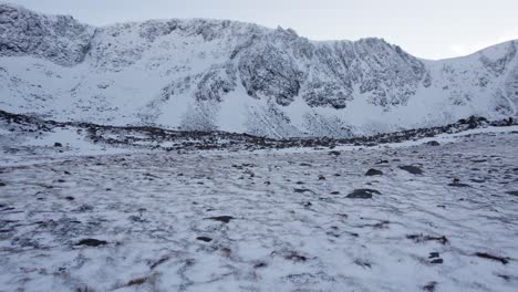 Rolling-aerial-drone-footage-close-to-the-ground-the-headwall-of-Coire-an-t-Sneachda-in-the-Cairngorm-mountains-of-Scotland-in-snow,-ice-and-full-winter-mountaineering-conditions-with-snow-and-ice