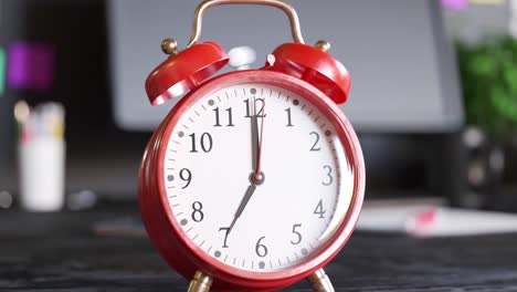 Old-vintage-red-alarm-clock-standing-on-a-wooden-office-desk.-Bells-ring-and-clock-shakes-on-time.-Office-workstation-in-a-background.-Symbol-of-morning,-countdown,-deadline.--Classic-ageless-design.