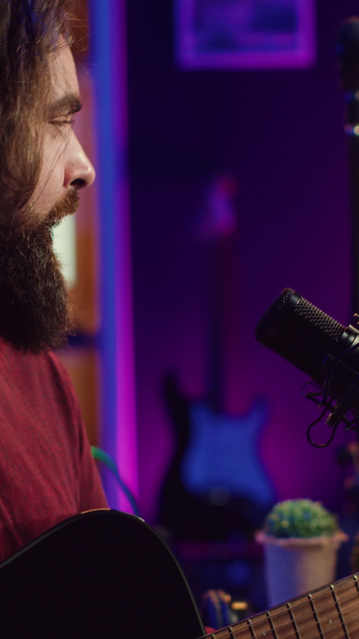 Uomo barbuto che suona la chitarra acustica e canta nel microfono in studio