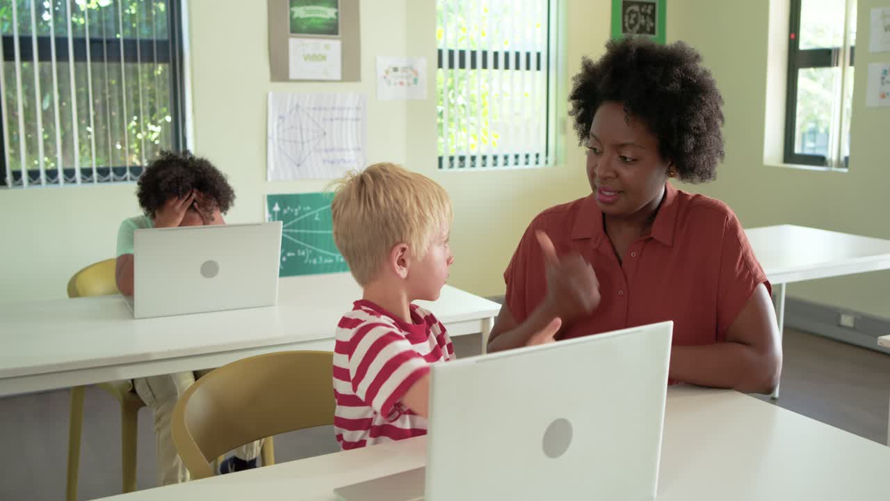 African teacher showing hand shapes guiding youth blond boy practicing signs in class on laptop