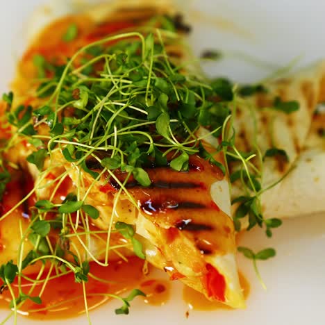 tasty appetizer. red sauce is pouring on a delicious cooked pita that is spinning on white plate. tasty dish with green sprouts in a restaurant