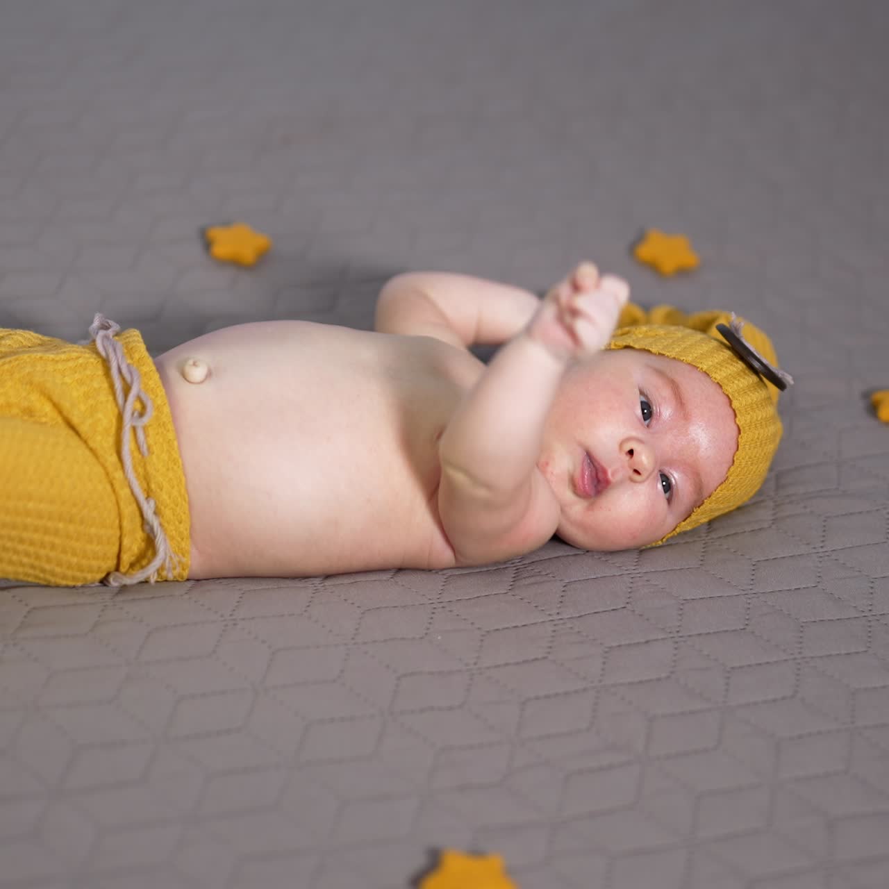 Cute tiny child moving his hands actively. Boy in yellow costume and surrounded by small toy stars on the grey blanket