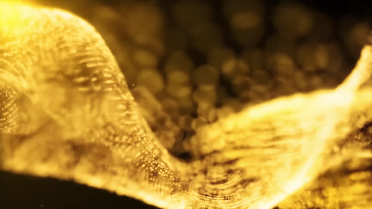 Golden particles flow gracefully, forming dynamic wave patterns against a dark background. The interplay of light and shadow enhances the visual richness and allure of the composition.
