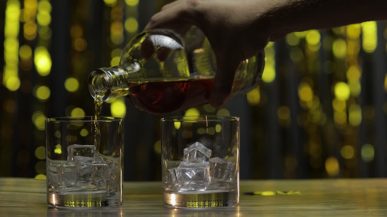 vertido de whisky, coñac o brandy de la botella en vasos con cubos de hielo. fondo brillante