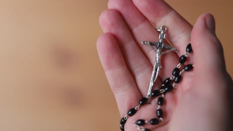 hand clasping and holding rosary beads with cross