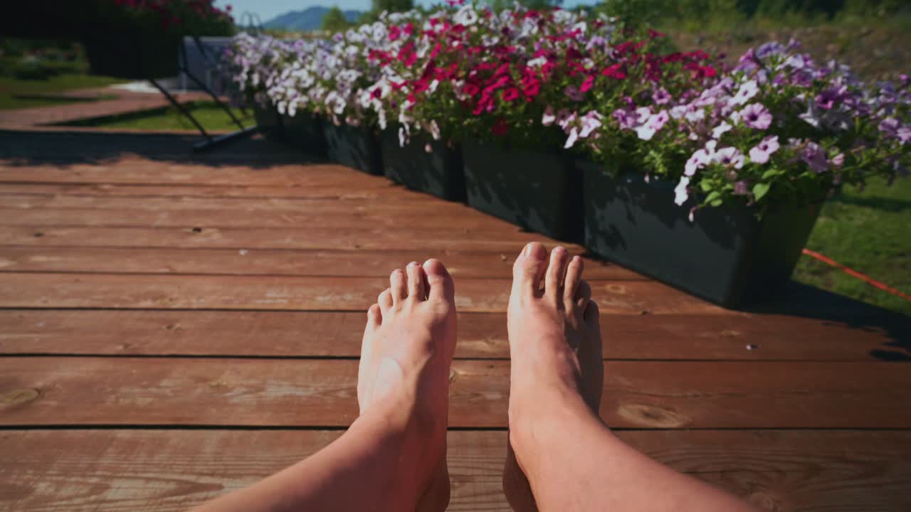 Vista in prima persona di piedi che si rilassano su una terrazza assolata con fiori