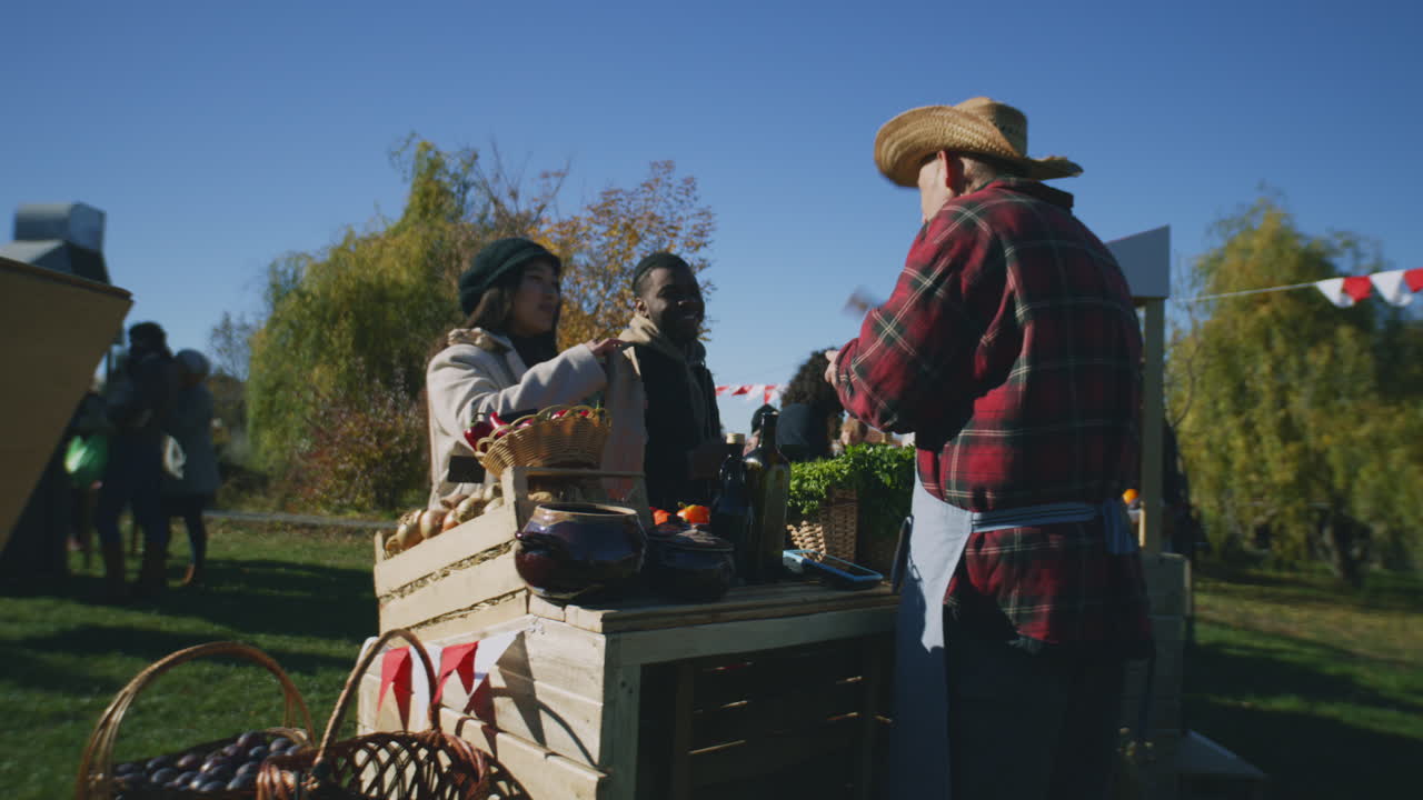 Couple Shopping at Local Farmers Market Couple Shopping at Local Farmers Market Man Contactless Pays for Purchases to Farmer Using Smartphone Autumn Fair Outdoors Vegetarian and Organic Food Agriculture Point of Sale system