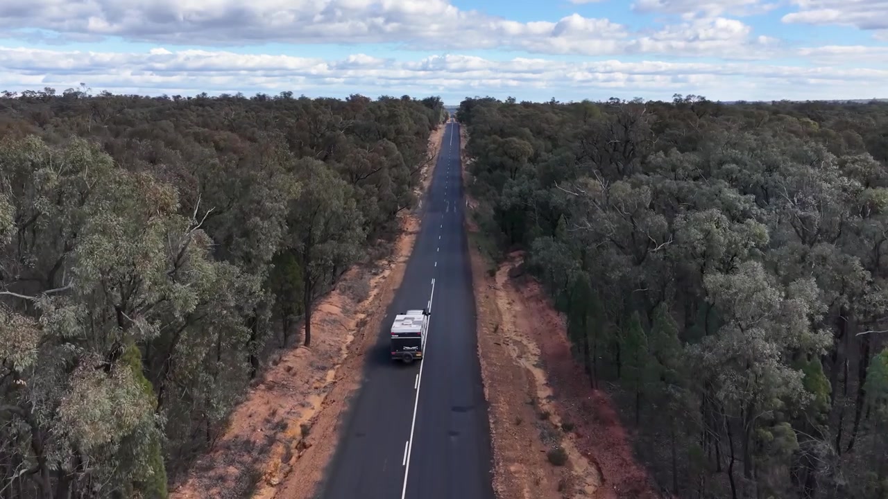 Un veicolo bianco traina una roulotte lungo una strada asfaltata dritta attraverso la fitta boscaglia australiana