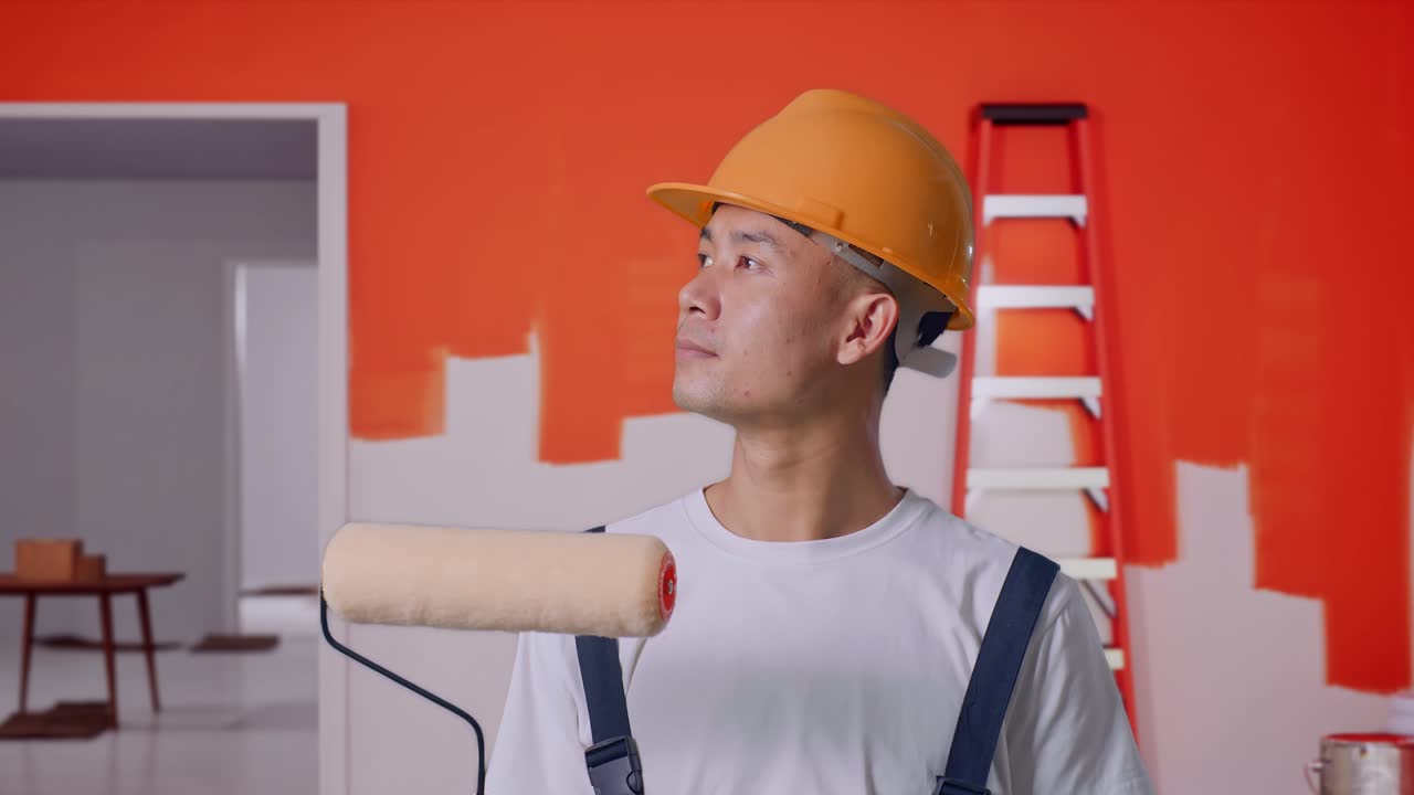 Close Up Of Asian Man Painter Wearing Safety Helmet Standing And Look Around With Painting Wall In Room