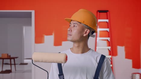 close up of asian man painter wearing safety helmet standing and look around with painting wall in room