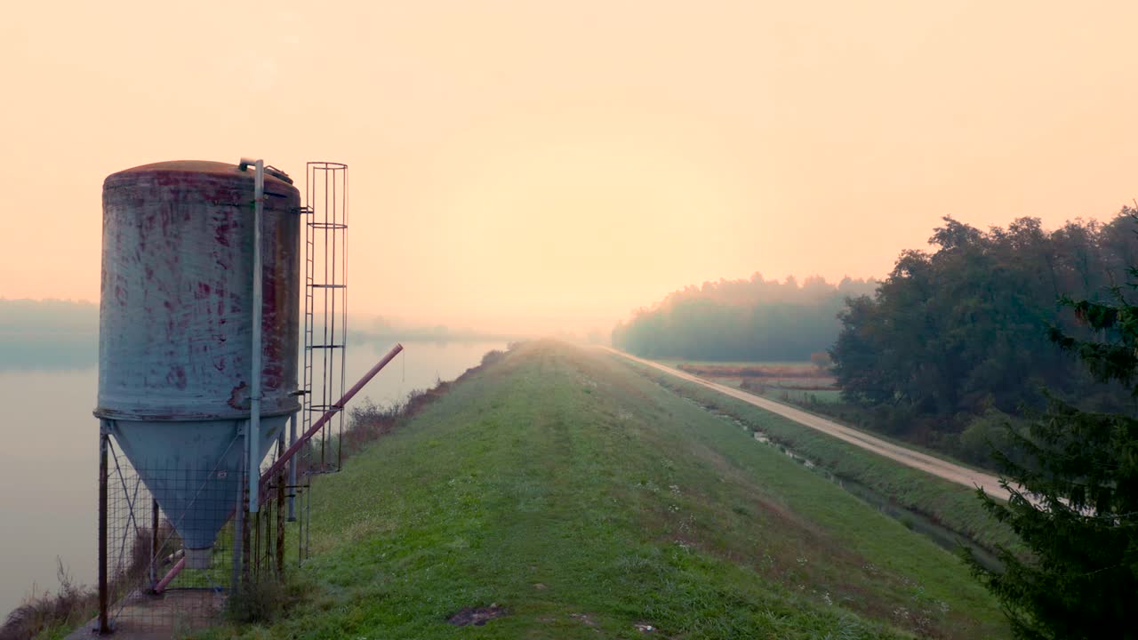 paisaje con un lago y silos para la alimentación de peces y una sola carretera que lo bordea en la brumosa mañana de otoño en europa central