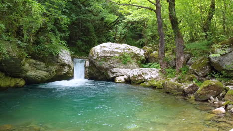 Bañada-Por-El-Brillo-Mágico-Del-Sol,-Una-Cascada-Cae-Río-Abajo,-Rodeada-De-Verdes-árboles-Forestales-Y-Exuberante-Vegetación,-Creando-Una-Encantadora-Escena-Natural-En-La-Cascada-De-Kouiassa,-Epiro.